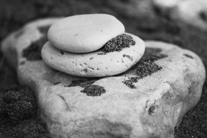 Black and white photograph of two smooth stones balanced one on top of the other on a larger rock.