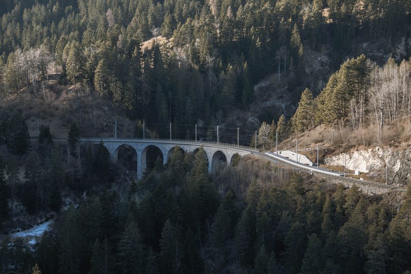 A stone railway viaduct with several arches crossing a forested mountain valley in low winter light.
