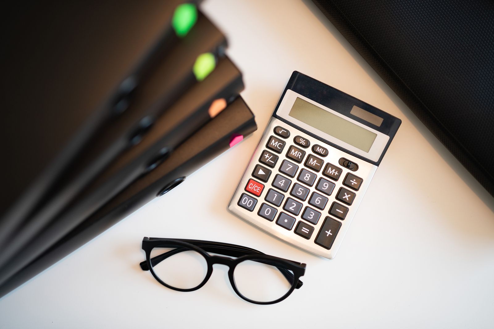 A calculator and reading glasses on a desk.