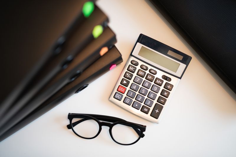 A calculator and reading glasses on a desk.